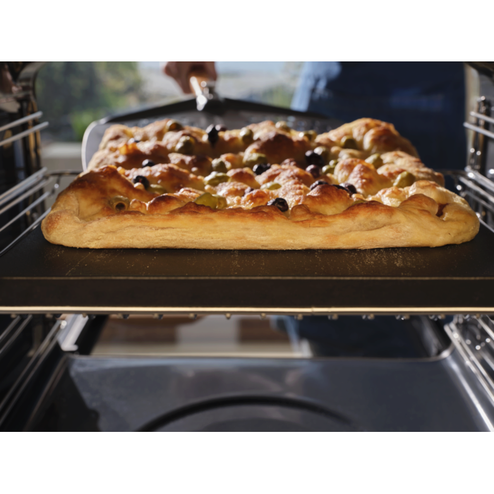 A focaccia baking inside the pizza expert oven with a pizza peel underneath 