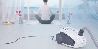 Žena cvičiaca jogu v popredí s vysávačom Electrolux Ultra Silencer