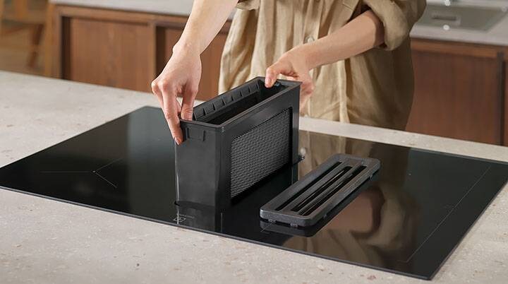 Hands putting back the grease filter on a  Extractor hob
