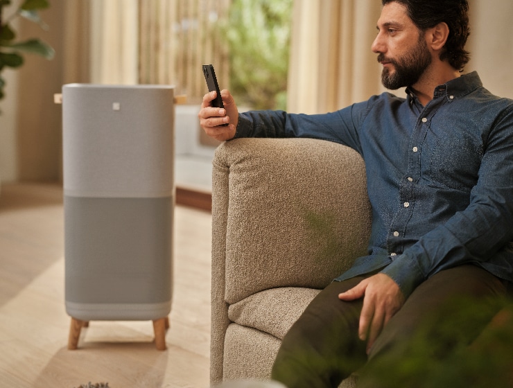 Muž sedí vedľa čističky vzduchu a drží telefón.