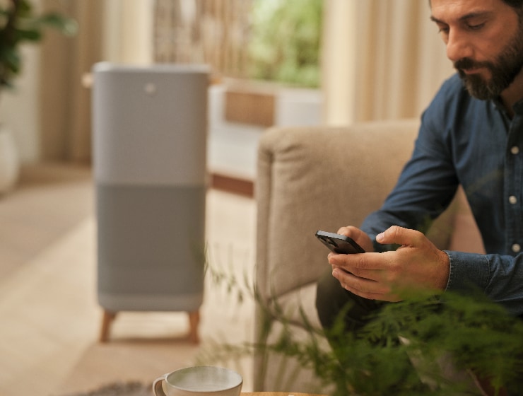 Muž sedí vedľa čističky vzduchu a drží telefón.