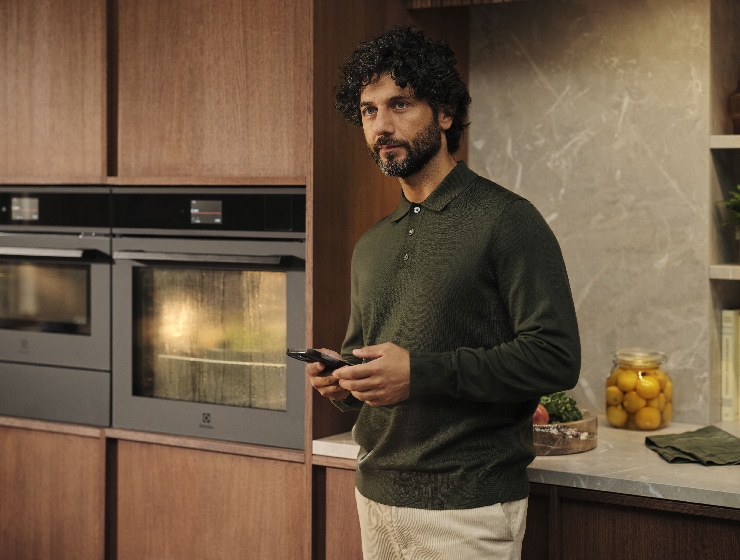 Muž stojaci v kuchyni a drží telefón.